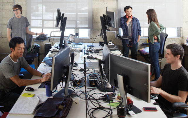 Un open space avec 5 personnes en train de travailler sur des ordinateurs